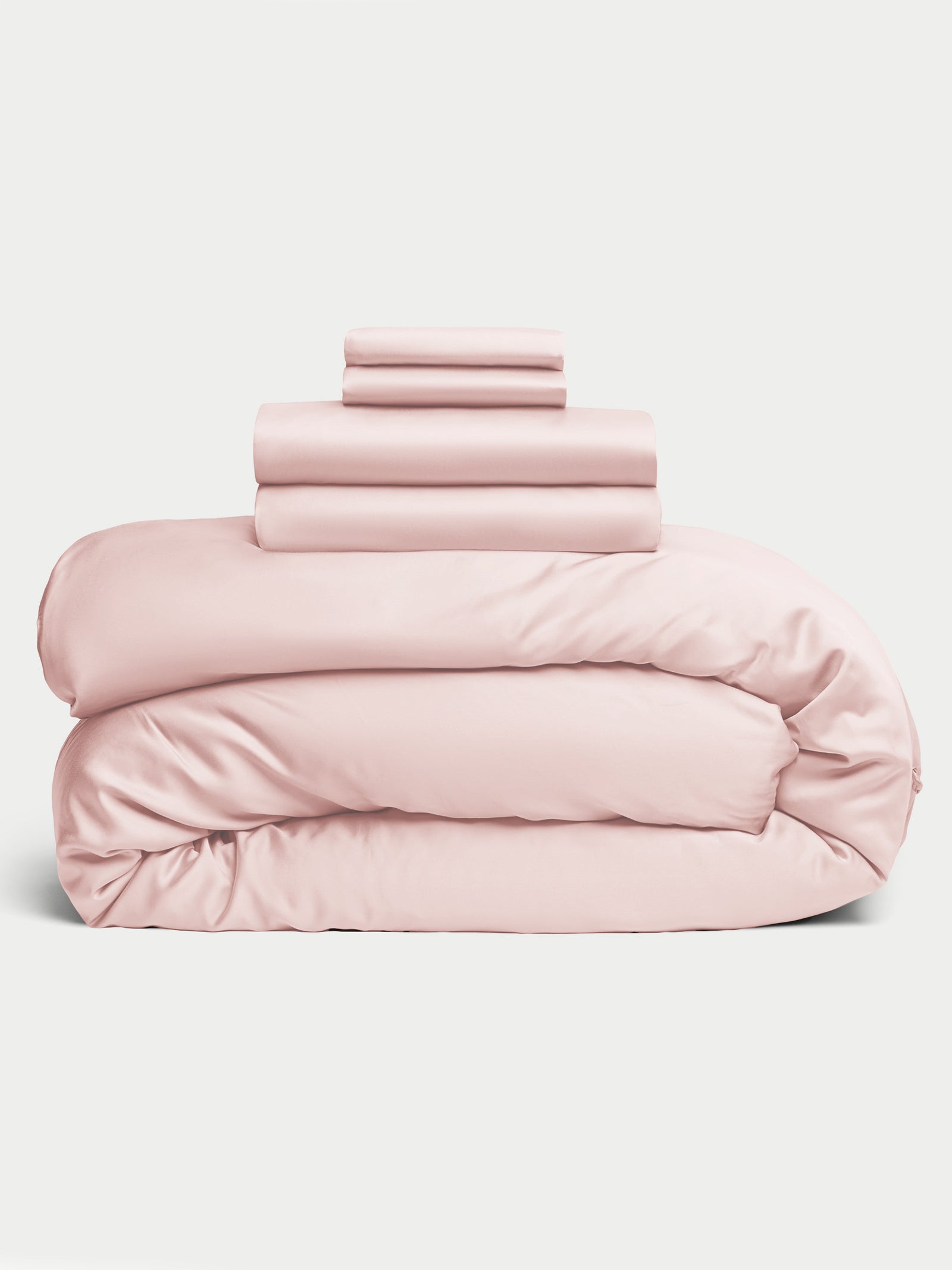 A neatly folded light pink Bamboo Bedding Deluxe Bundle by Cozy Earth, including a comforter, sheets, and pillowcases, stacked in a tidy pile on a plain background. 