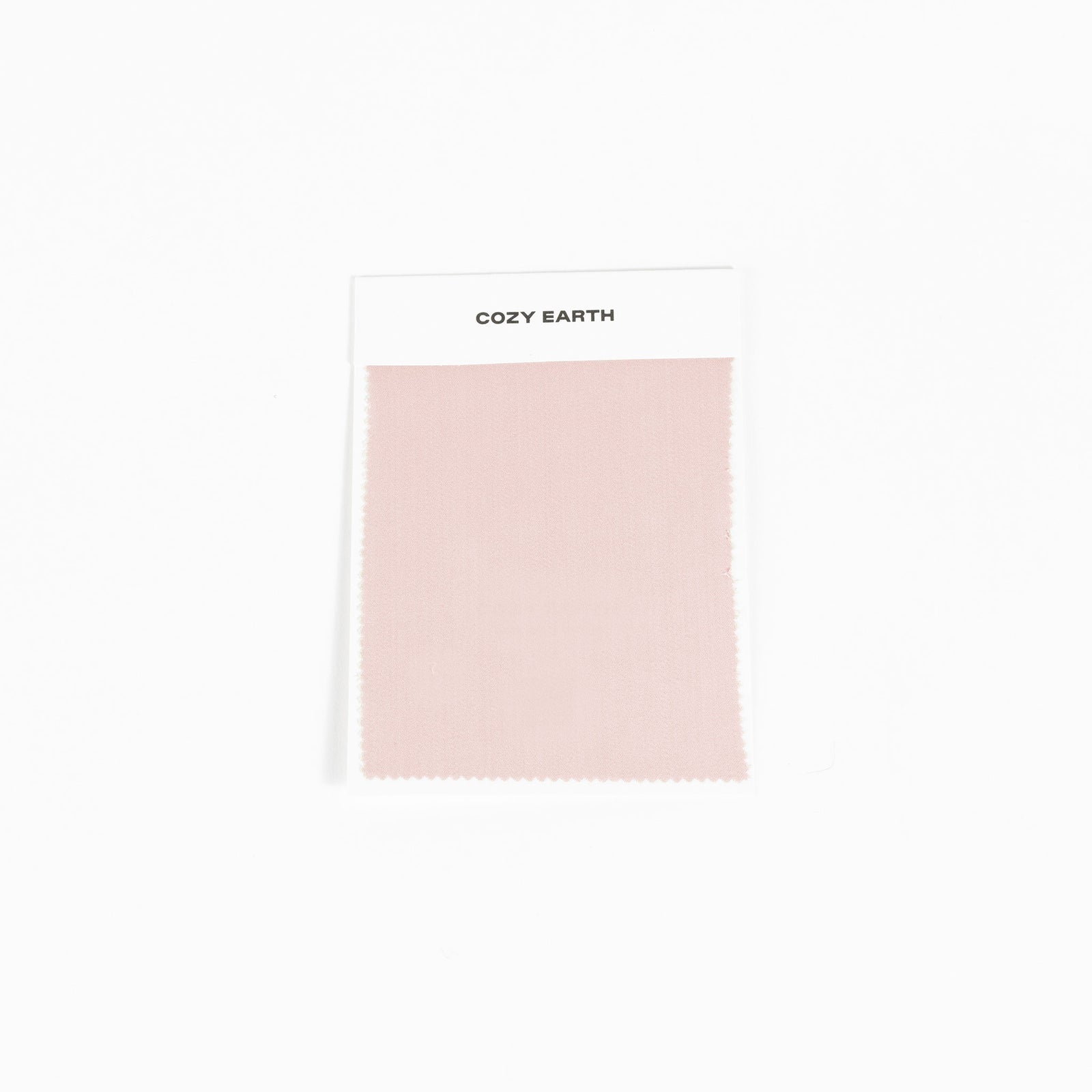 A sample swatch of Bamboo Sheet fabric from Cozy Earth, in light pink, is displayed on a white card against a white background.