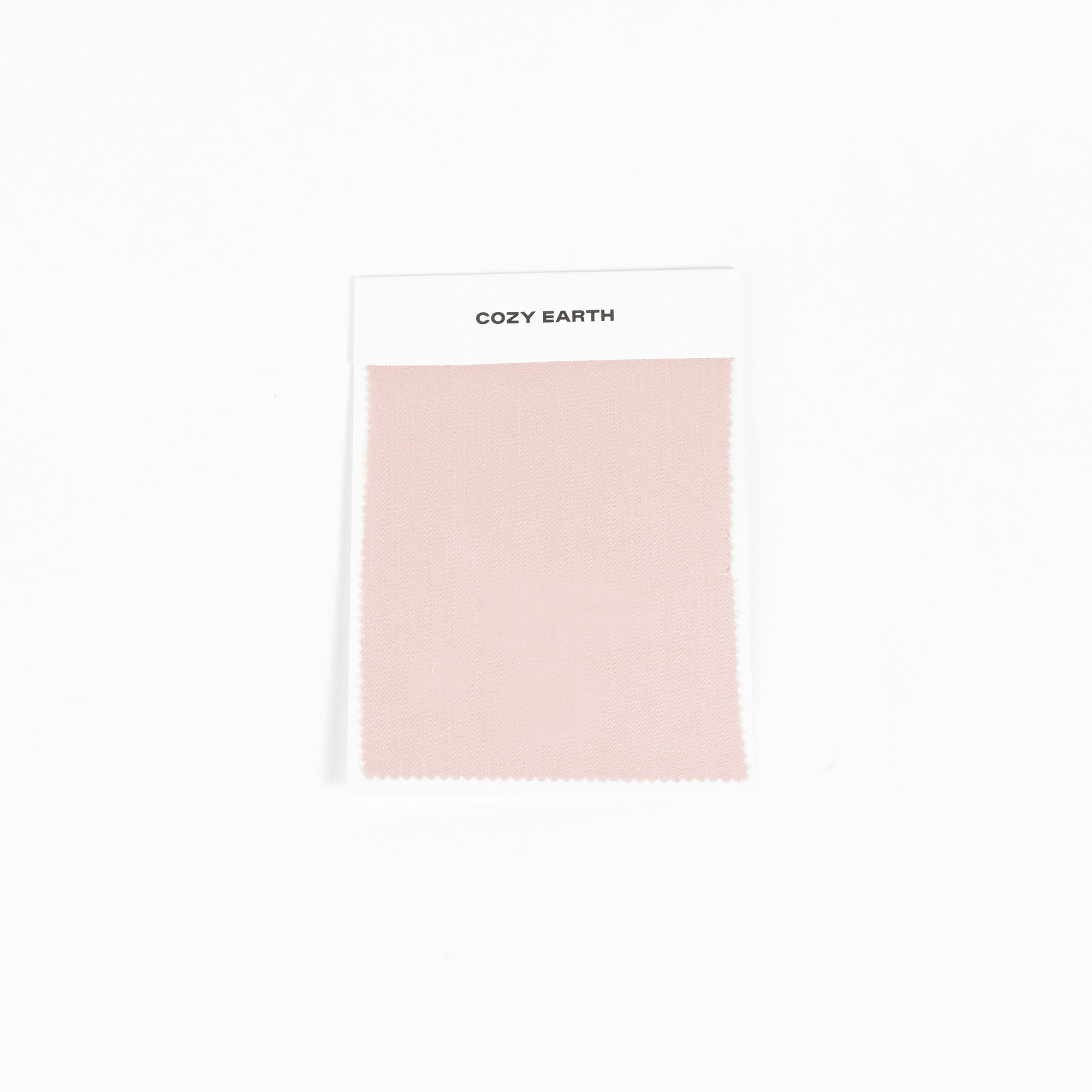 A sample swatch of Bamboo Sheet fabric from Cozy Earth, in light pink, is displayed on a white card against a white background.