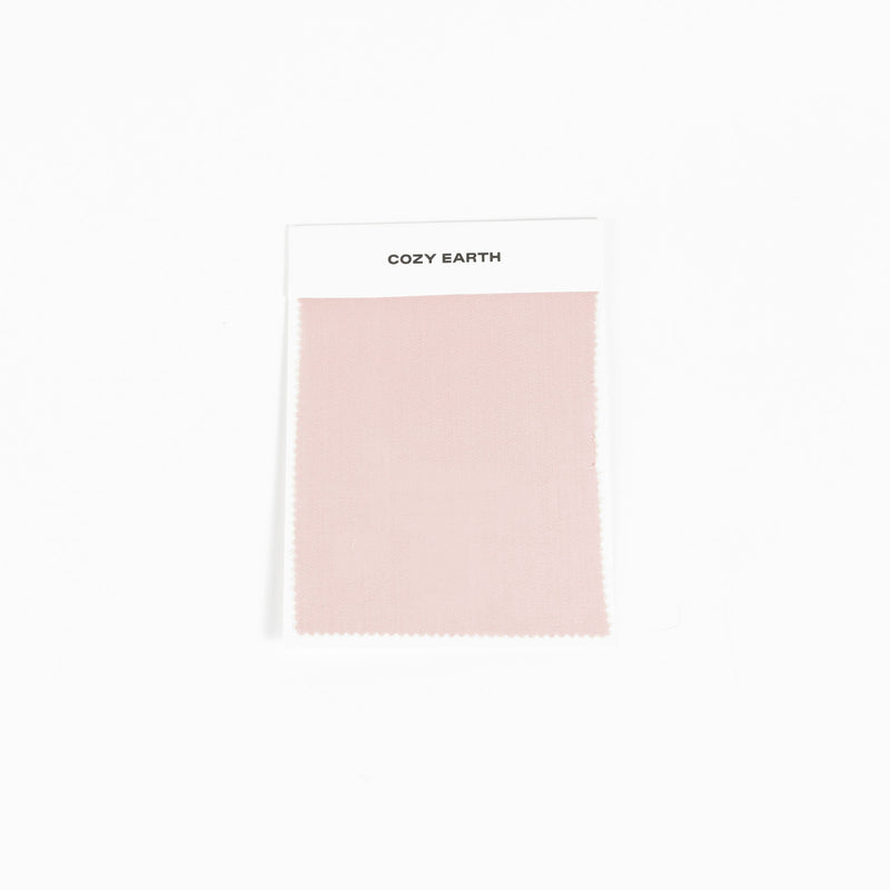 A sample swatch of Bamboo Sheet fabric from Cozy Earth, in light pink, is displayed on a white card against a white background.