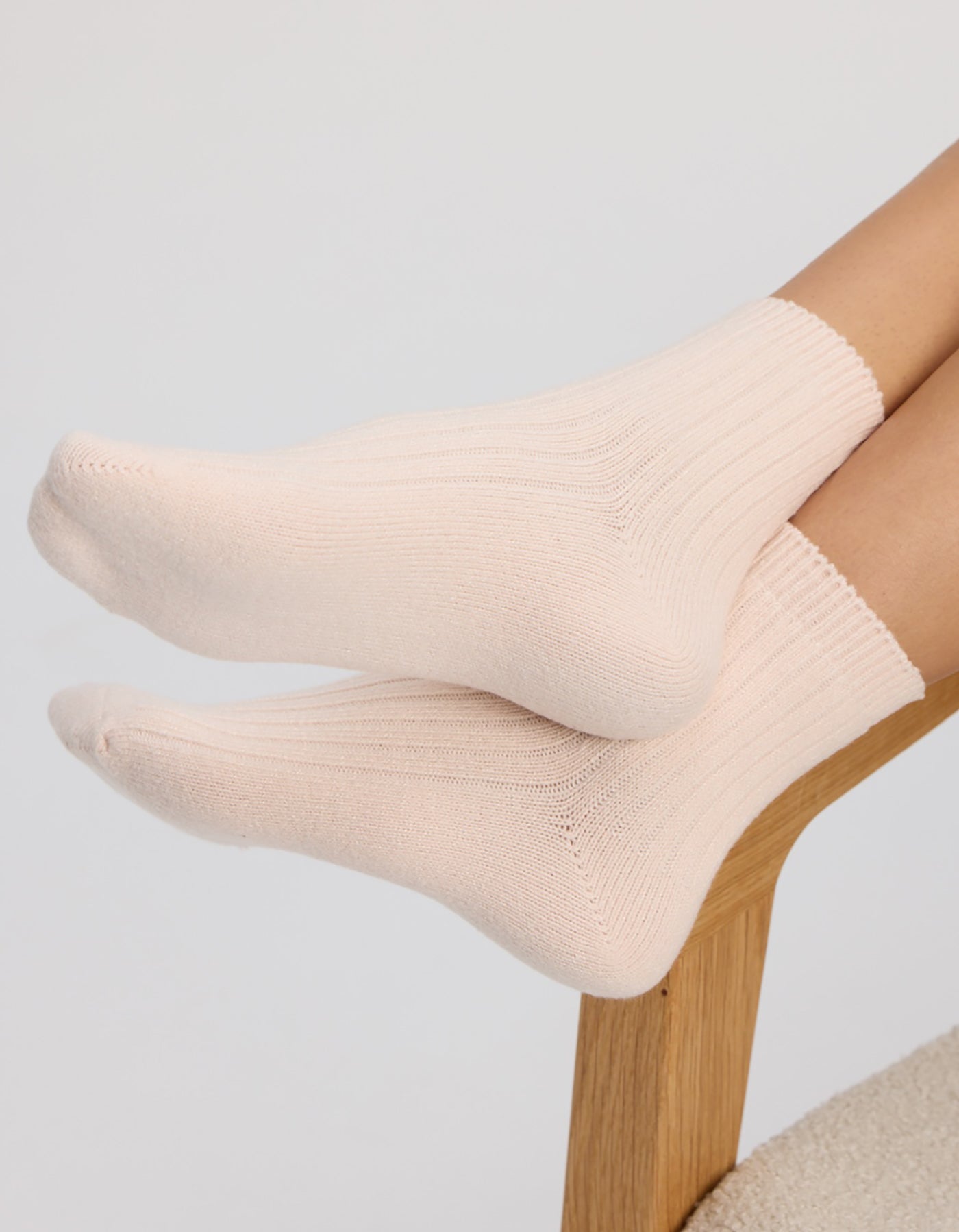 A person wearing Cozy Earth's Plush Modern Crew Sock in light pink rests their feet on the curved seat of a wooden chair against a plain background.