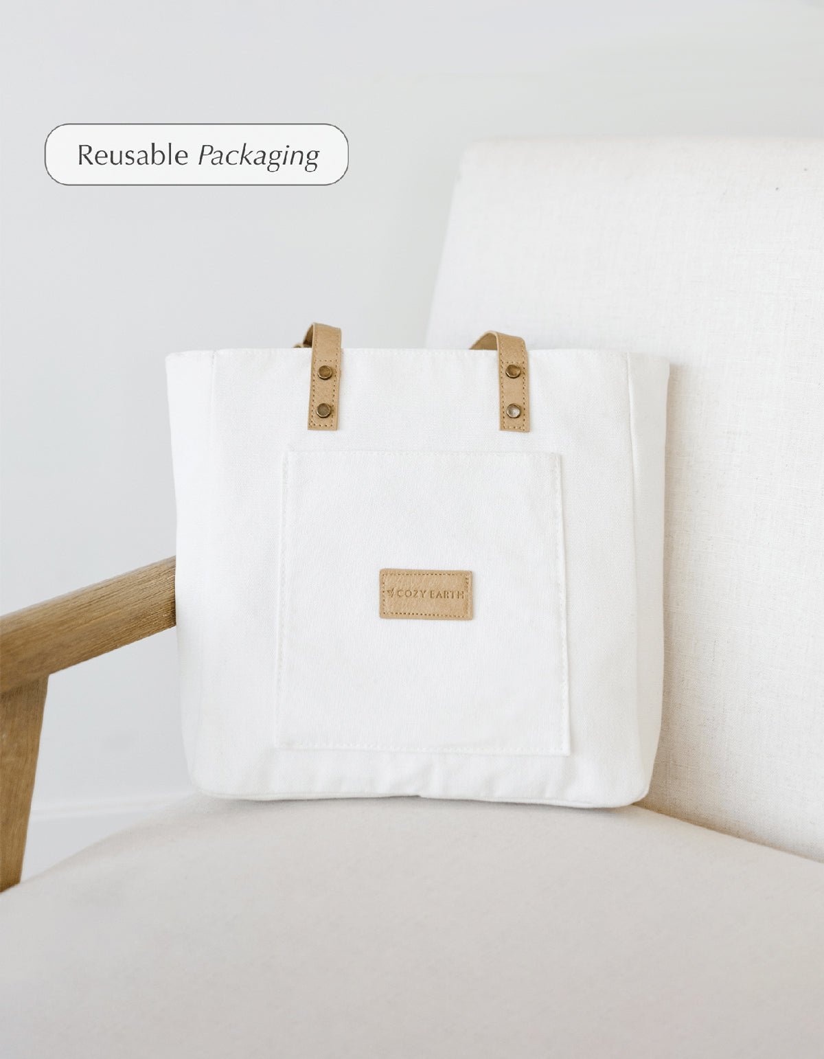 A Cozy Earth Tote Bag containing Bamboo Sheet Set sits on a creme chair. Driftwood, Light Grey, White, Oat, Shore, Creme, Charcoal, Dove Grey, Pacific Blue, Peony, Walnut, Laurel, Lavender