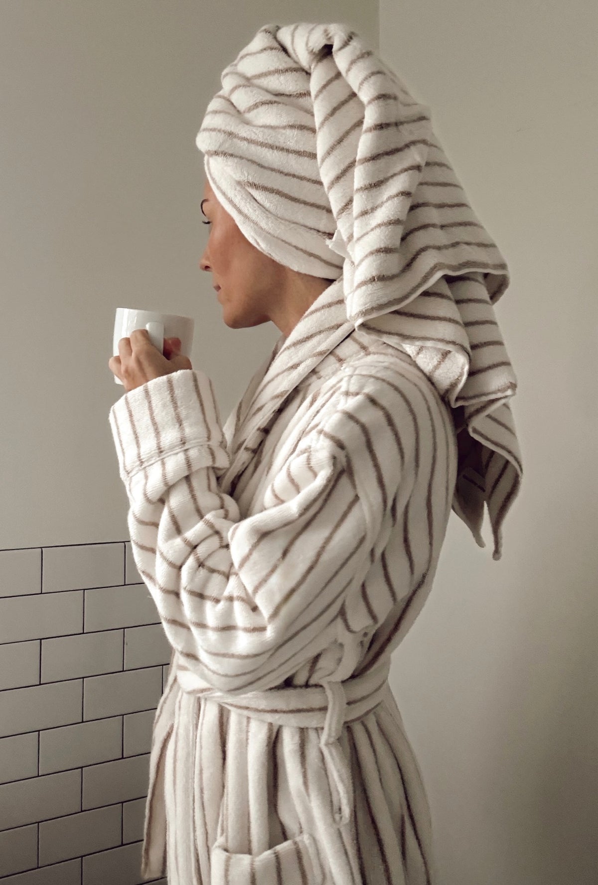 Woman in a striped robe with a hair towel wrapped up, holding a mug