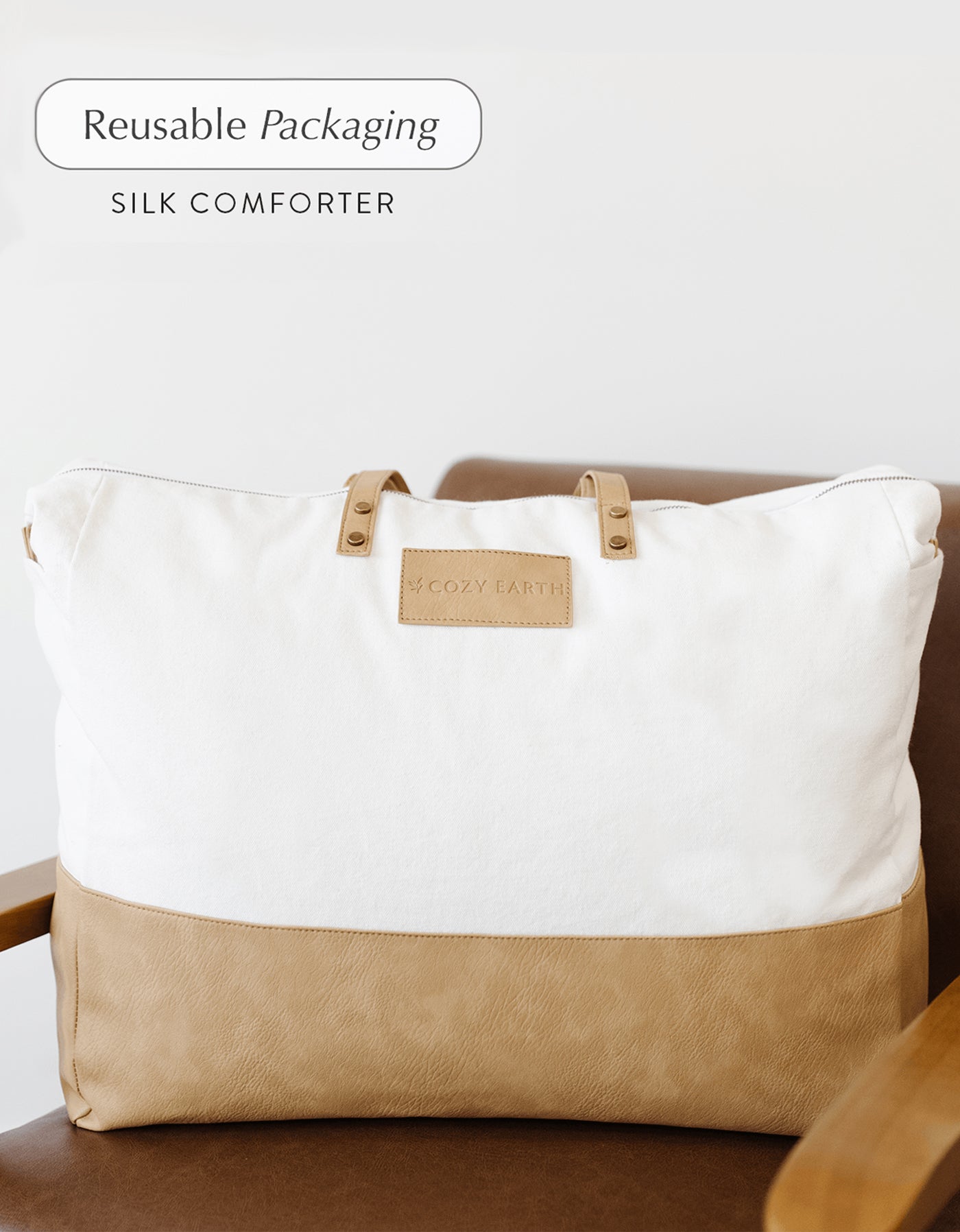 A large beige and white fabric bag labeled "Cozy Earth" with the text "Reusable Packaging, Silk Comforter" sits on a brown chair.