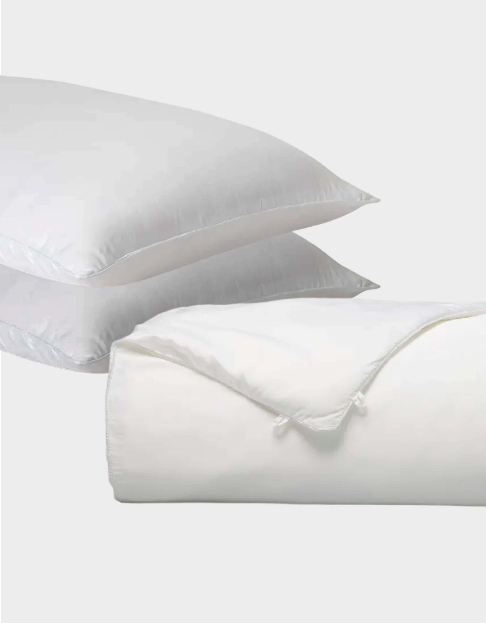 Two white Cozy Earth Silk Insert Bundle pillows are stacked, with a folded comforter featuring a tied corner in front, all set against a plain light gray background.