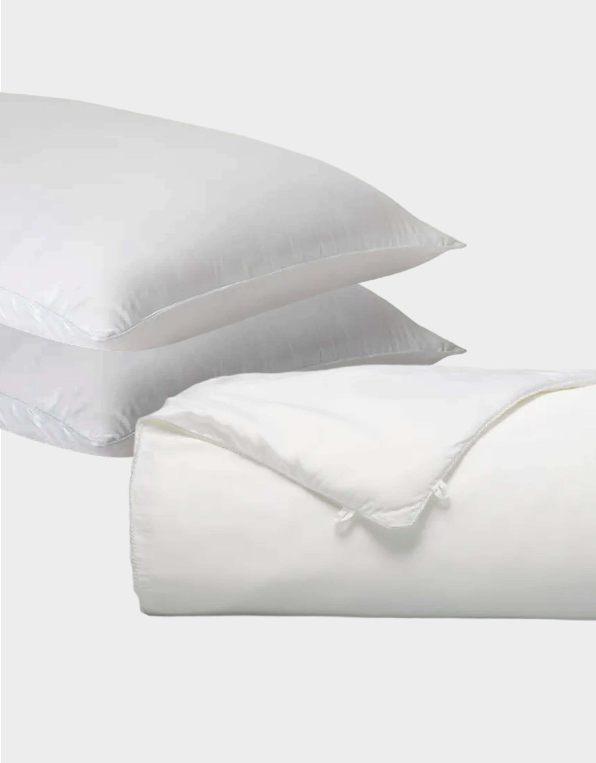 Two white Cozy Earth Silk Insert Bundle pillows are stacked, with a folded comforter featuring a tied corner in front, all set against a plain light gray background.