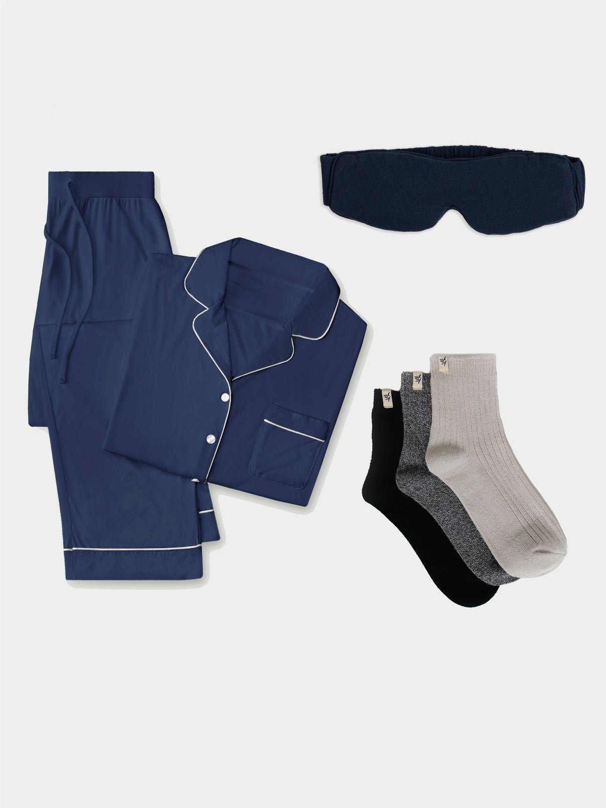 The Women's Bedtime Bundle by Cozy Earth in navy includes a button-up pajama shirt with white piping and a chest pocket, along with matching pants. The set is completed with a black sleep mask and three pairs of socks in heather grey, black, and light grey. |Color:Navy