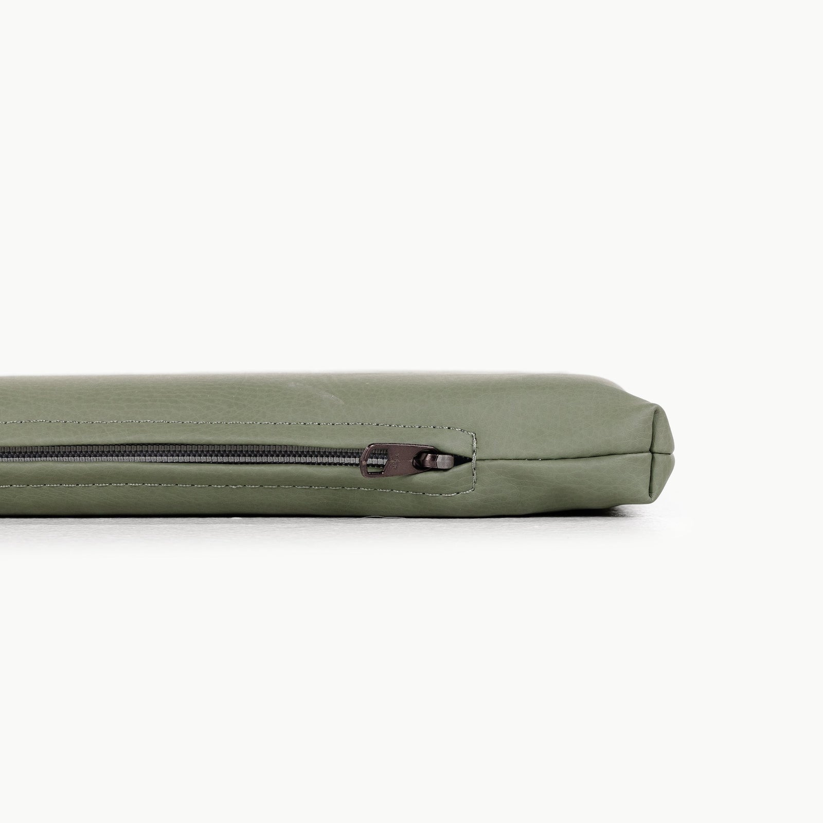 A close-up side view of the Gathre Wholesale Padded Changing Mat in light green shows only its top edge and visible zipper as it rests on a white surface.
