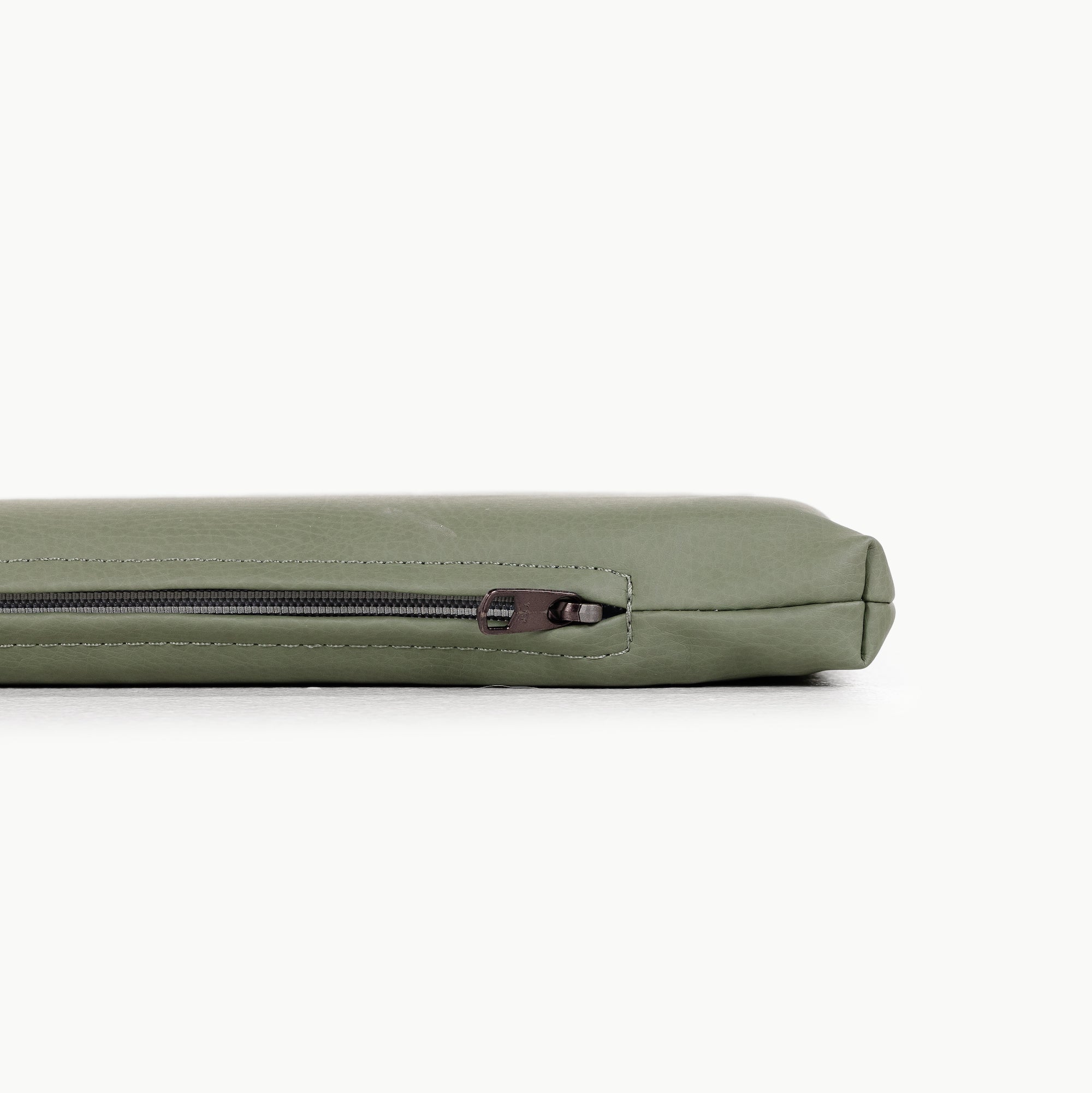 A close-up side view of the Gathre Wholesale Padded Changing Mat in light green shows only its top edge and visible zipper as it rests on a white surface.