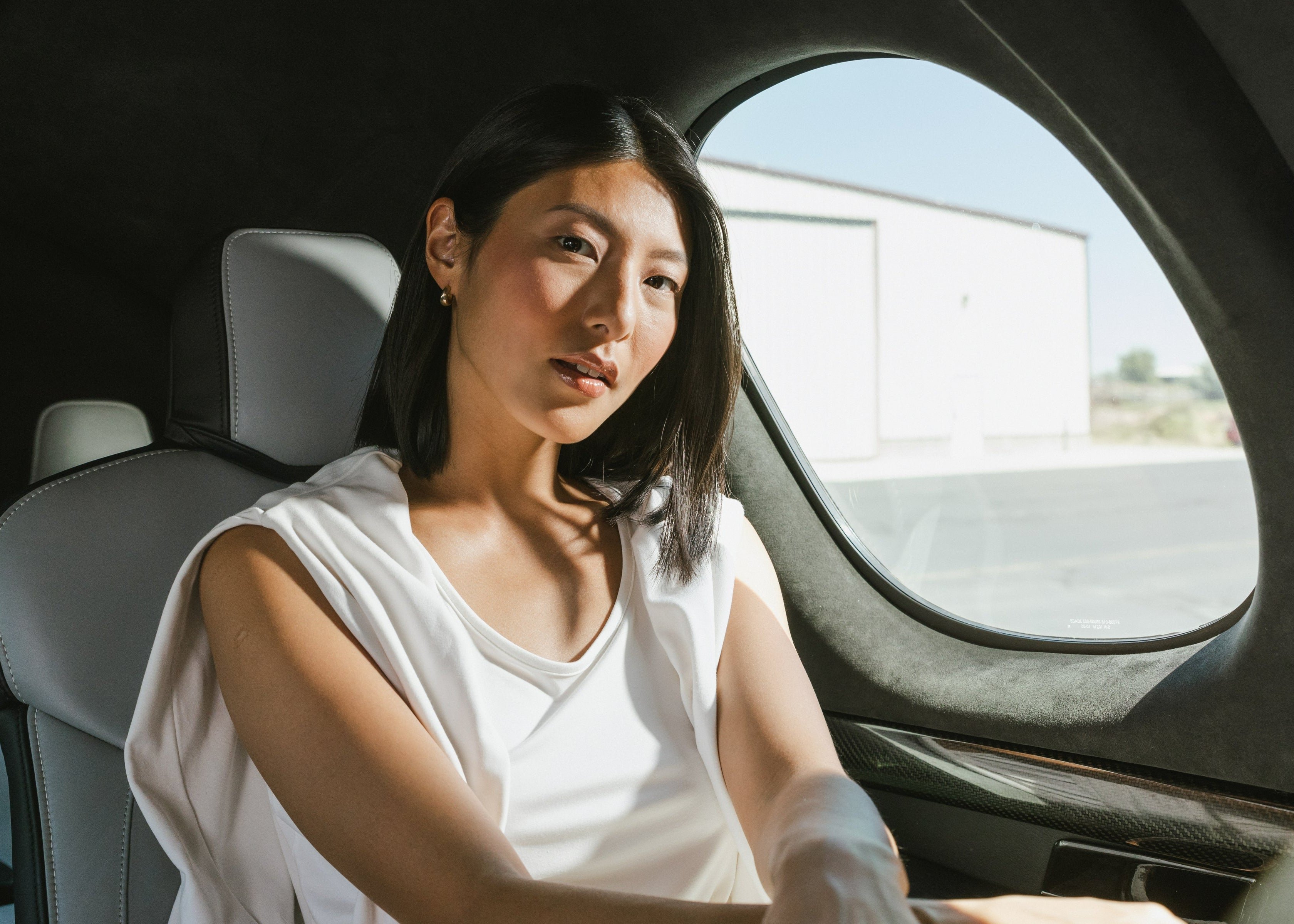 Woman sitting inside a vehicle with a clear sky and road visible through the window.