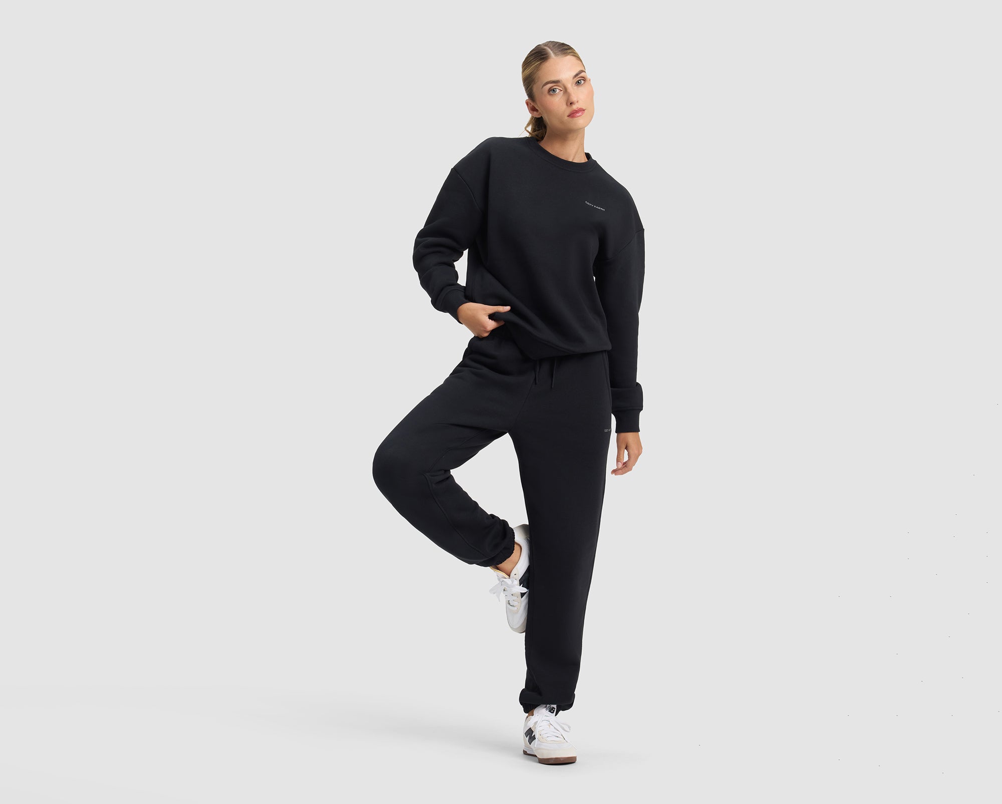 A woman wear Cozy Earth Cityscape 2.0 Crewneck & Sweatpant set in black. She stands in front of a white background.