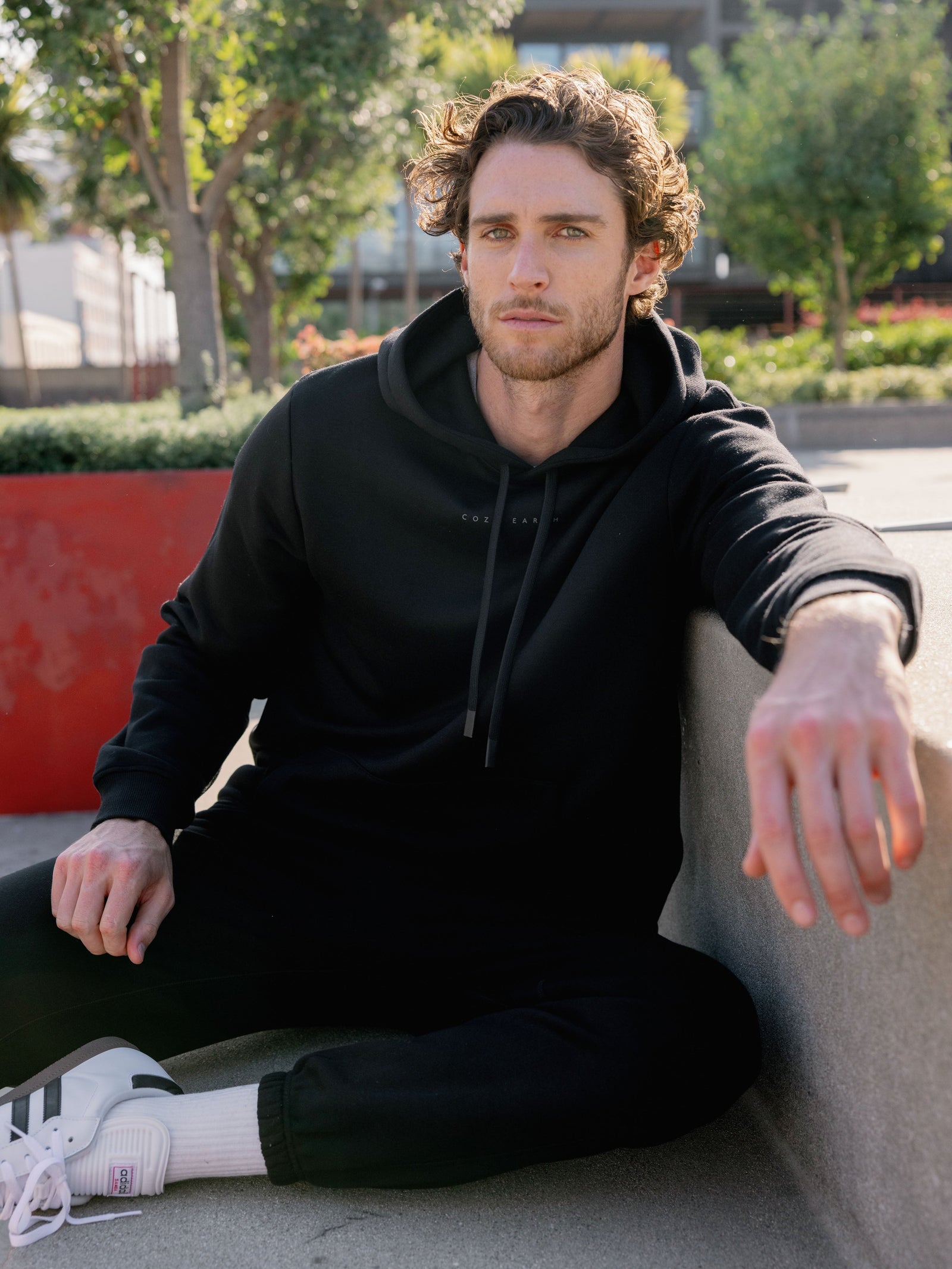 Man sitting on city bench wearing black cityscape hoodie and sweats 