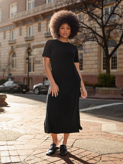Black Bamboo Midi Dress modeled by a woman. The photo was taken in a high contrast setting, showing off the colors and lines of the dress. |Color: Black