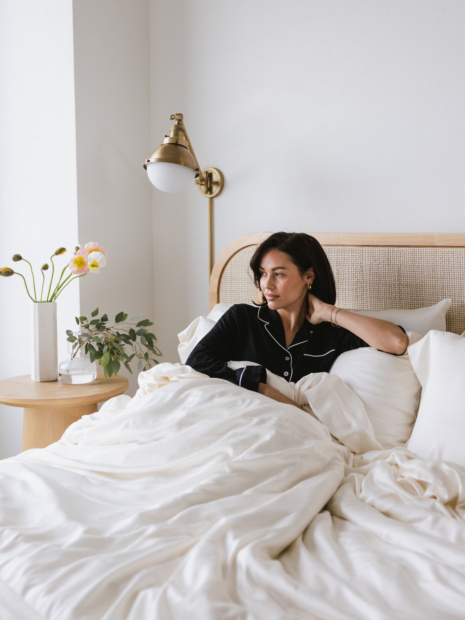Woman in black pajamas laying in bed with creme bedding 