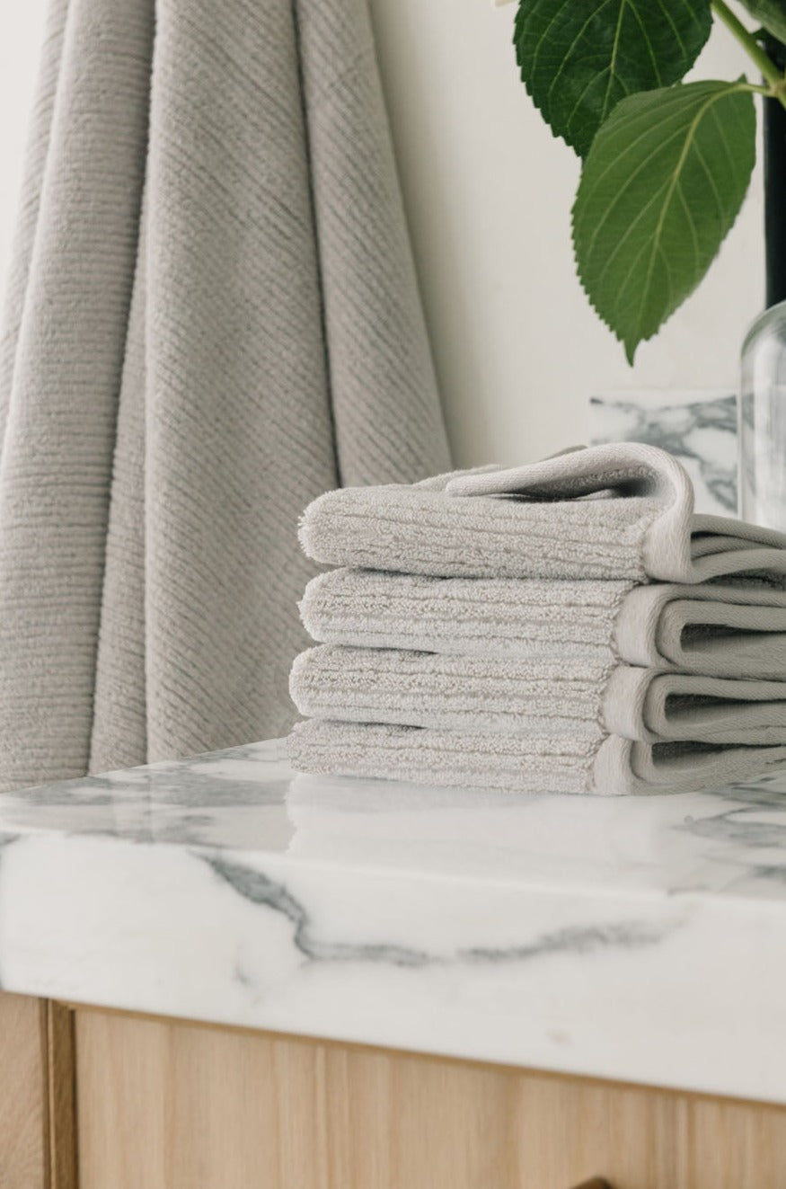 Ribbed Terry Wash Cloths in the color Light Grey. Photo of product taken on a white marble sink. 