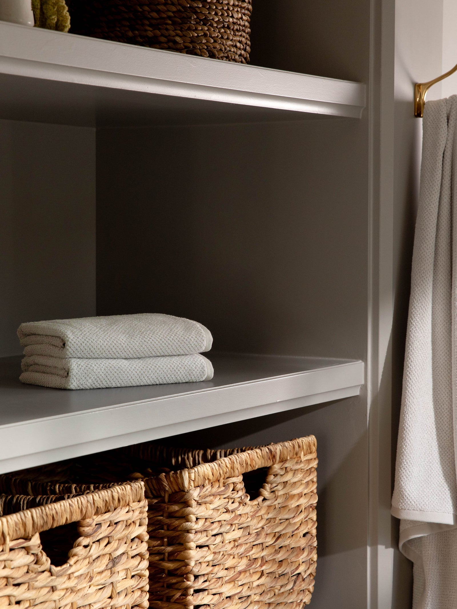 Nantucket Hand Towels in the color Heathered Light Grey. Photo of Nantucket Hand Towels taken with the hand towels resting on a shelf in a bathroom. 