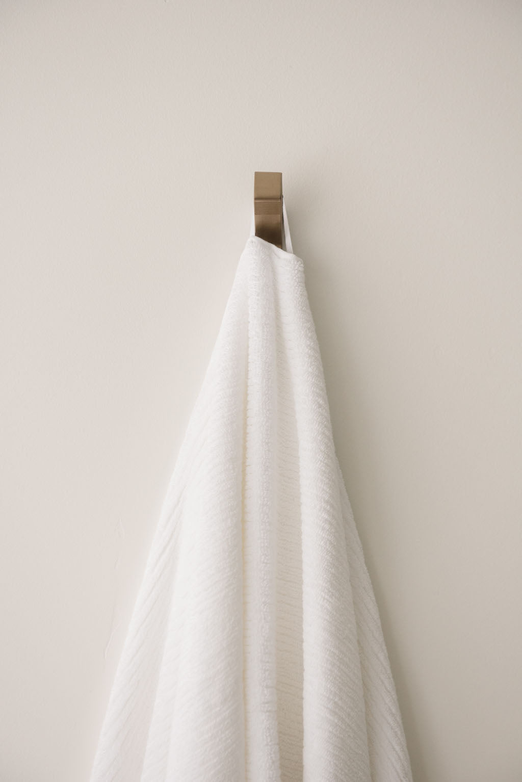 Ribbed Terry Bath Towel in the color White. Photo of Ribbed Terry Bath Towel taken as the White Ribbed Terry Bath Towel is hanging from a towel hook in a bathroom. 