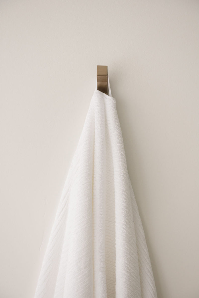 Ribbed Terry Bath Towel in the color White. Photo of Ribbed Terry Bath Towel taken as the White Ribbed Terry Bath Towel is hanging from a towel hook in a bathroom.