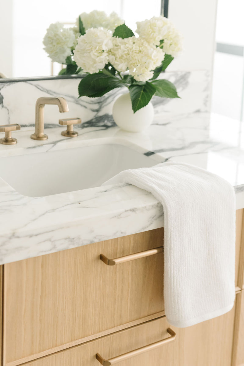 Ribbed Terry Hand Towels in the color White. Photo of product taken with the product draped over a white marble sink.