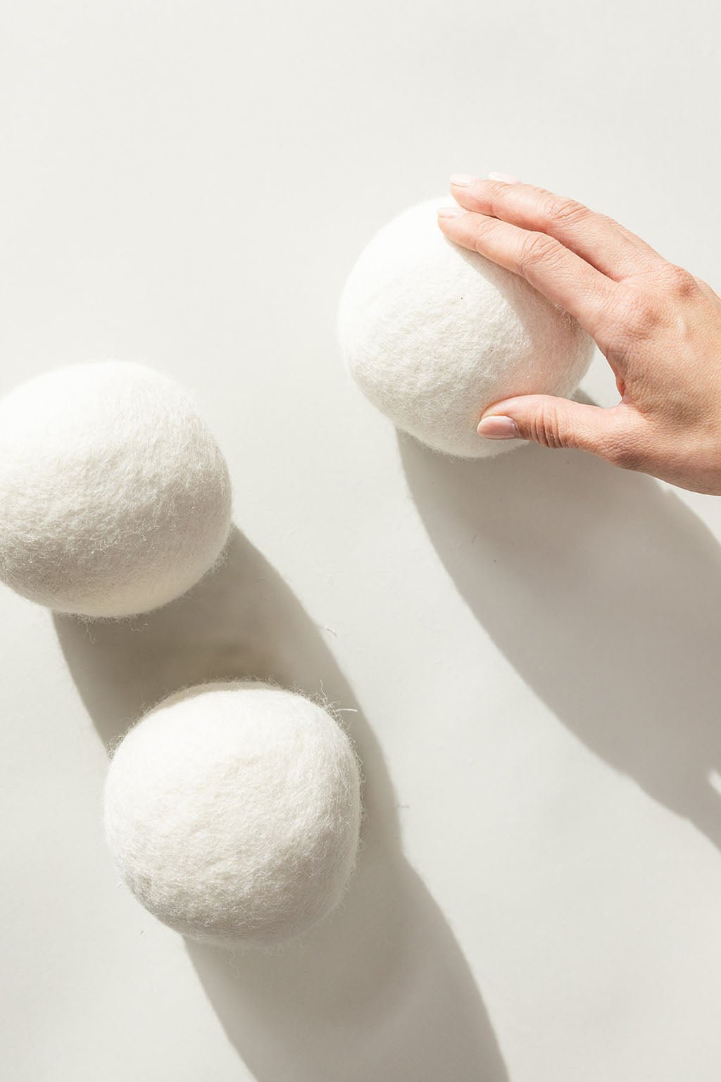 Wool Dryer Balls resting on a white background. A hand is feeling one of the wool balls.