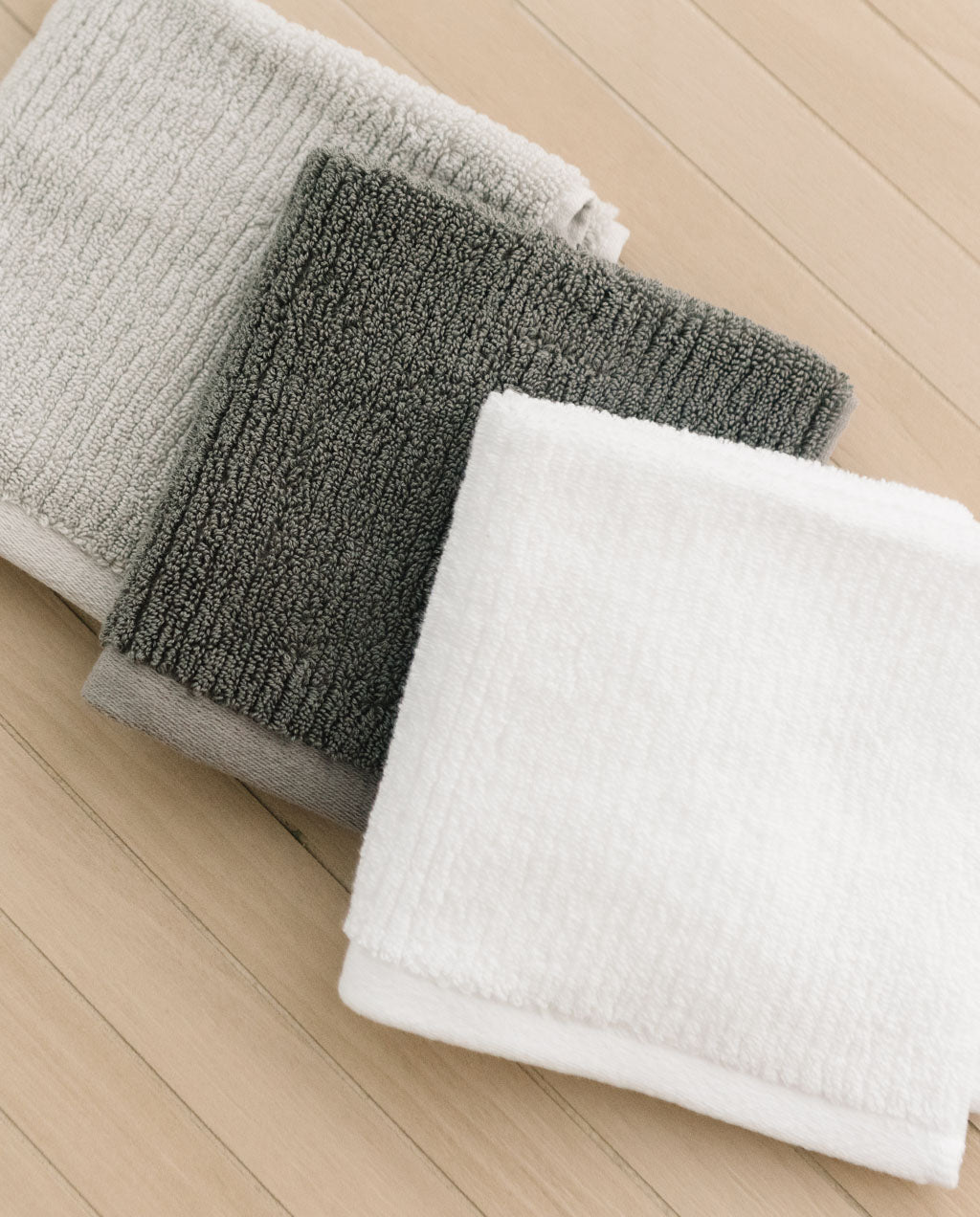 Charcoal White Light Grey Ribbed Terry Wash Cloths resting on a wood surface.
