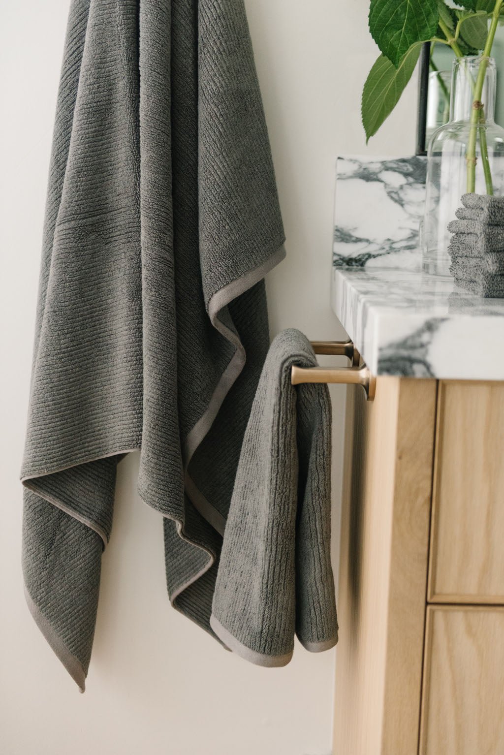 Ribbed Terry Hand Towels in the color charcoal. Photo of product taken with the product draped over a towel bar on the side of a white marble sink. |Color:Charcoal