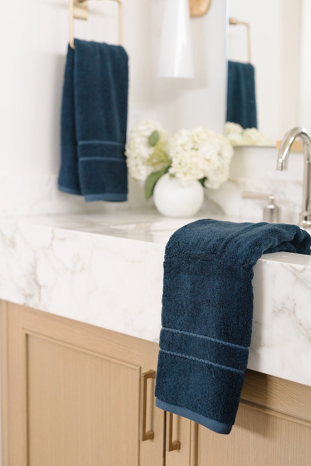 Premium Plush Hand Towel in the color Dusk. Photo of Dusk Premium Plush Hand Towel taken in a bathroom. one Premium Plush Hand Towel is hanging from a towel ring while the other is resting on the sink in the bathroom. |Color:Dusk