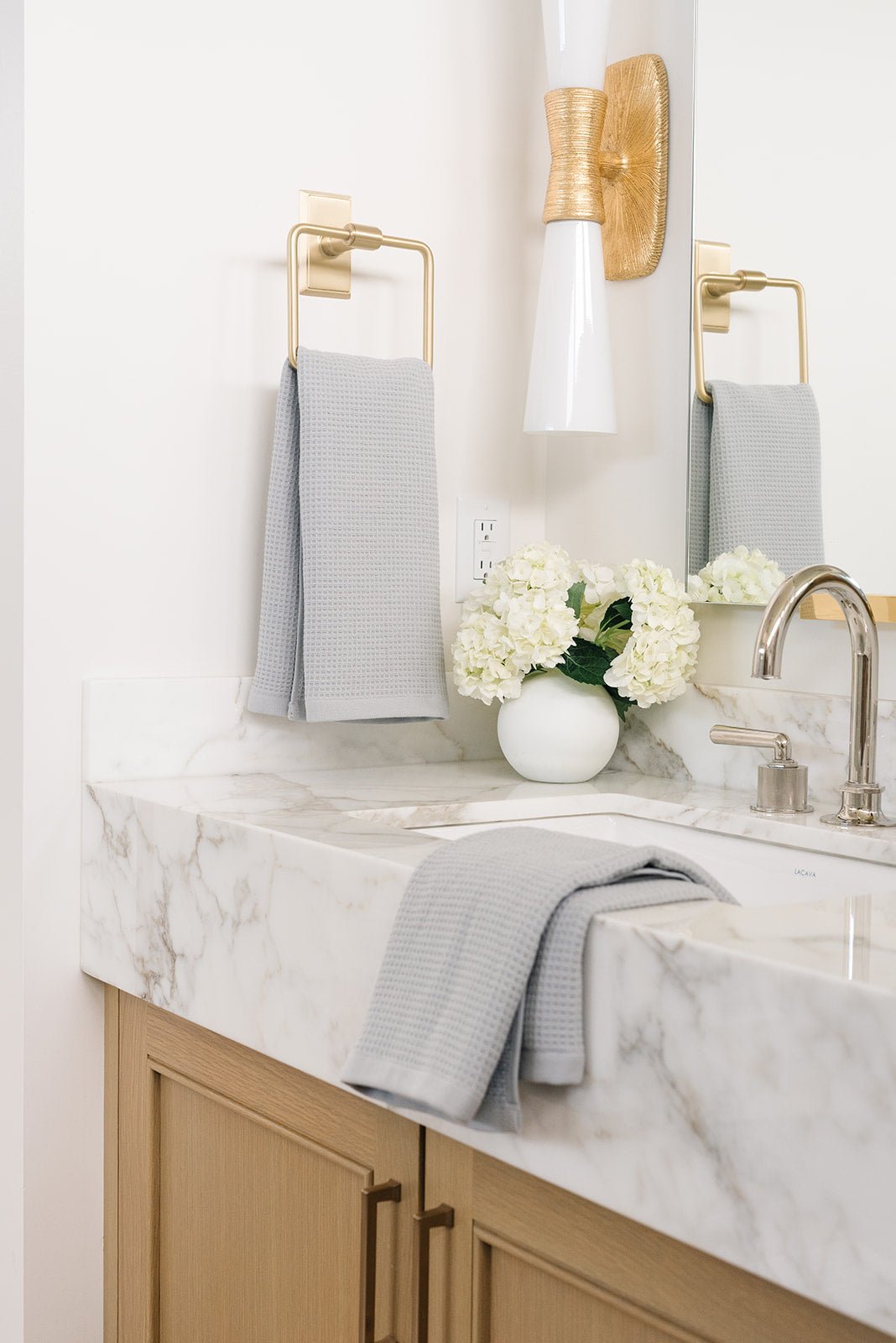 Harbor Mist Waffle Hand Towel hanging from a gold towel ring.  The photo was taken at a white marble bathroom sink. Another Hand Towel is resting on the sink. 