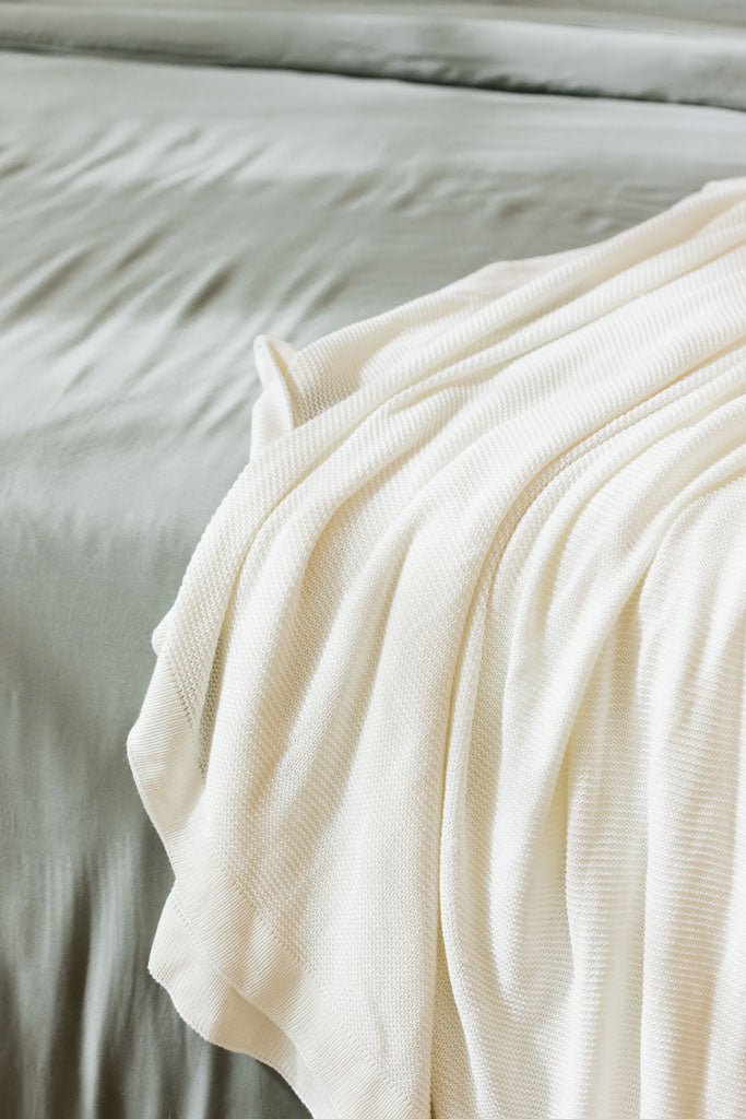 Ivory cloud knit blanket sitting on bed 