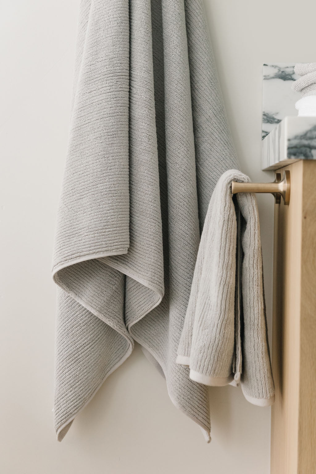 Ribbed Terry Hand Towels in the color Light Grey. Photo of product taken with the product draped over a towel bar on the side of a white marble sink. |Color:Light Grey
