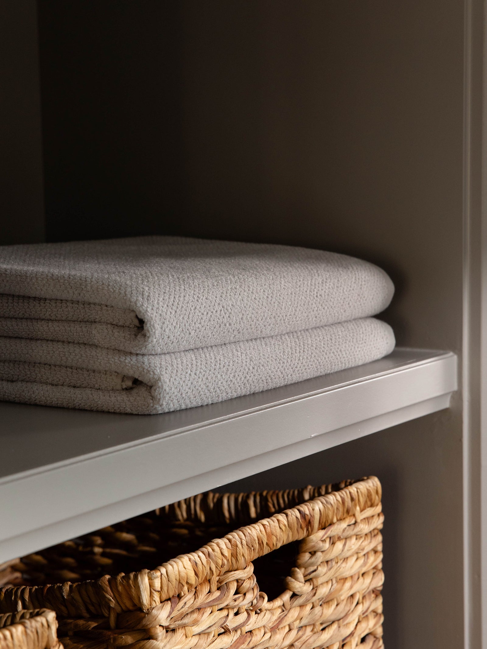 Nantucket Bath Towels in the color Heathered Light Grey. Photo of Nantucket Bath Towels taken as the towels rest on a shelf in a bathroom. 