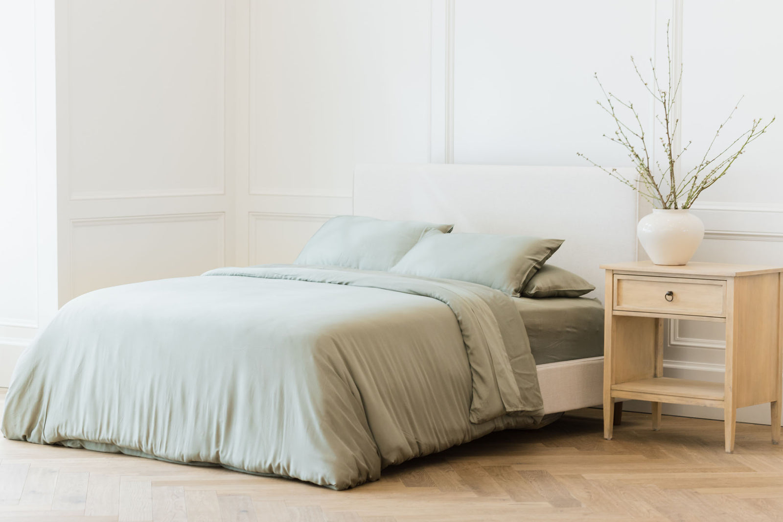 Zoomed out image of bed made with sage bedding in white bedroom 