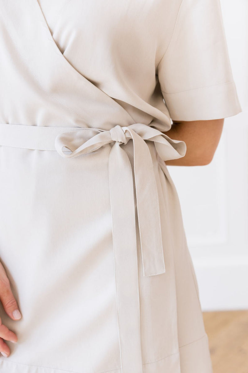 Close-up of a person wearing the Women's Cozy Earth Coastal Comfort Wrap Dress tied with a bow at the waist. The individual, captured standing sideways, rests their left hand gently on the back of their hip. The minimal and bright background highlights the fine details of this Cozy Earth dress.