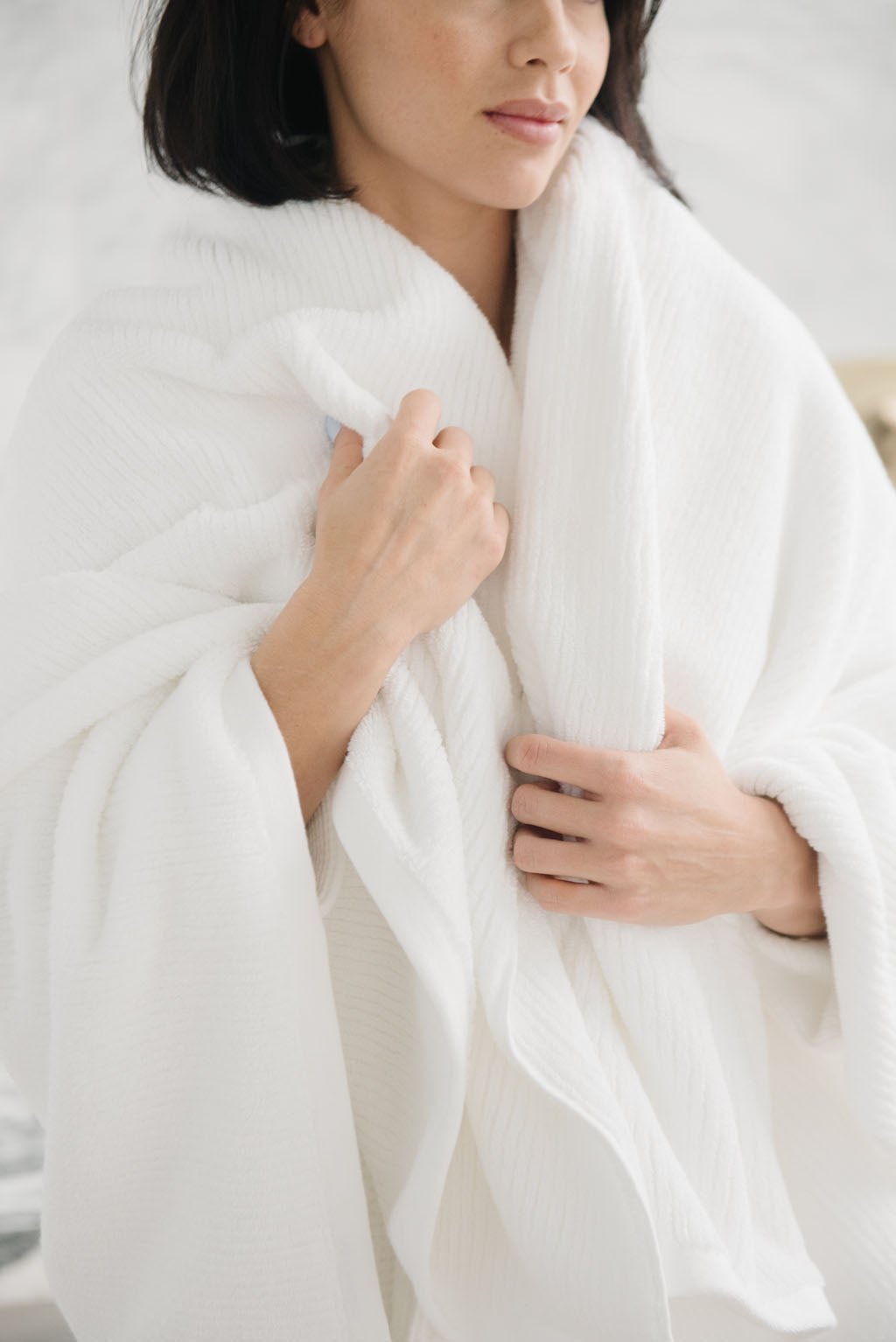 Ribbed Terry Bath Sheets in the color White. Photo of product taken in a bathroom as a woman wears the towel. 