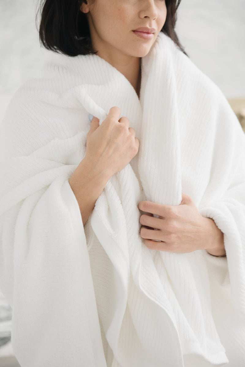 Ribbed Terry Bath Sheets in the color White. Photo of product taken in a bathroom as a woman wears the towel.