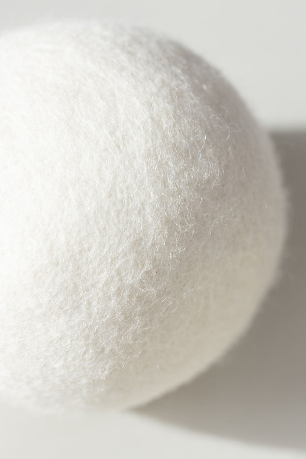Close up of a single wool dryer ball resting on a white background.