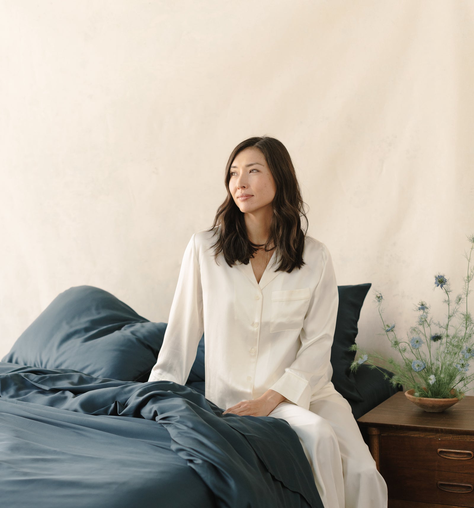 Woman in white pajamas sitting on bed with navy bedding 