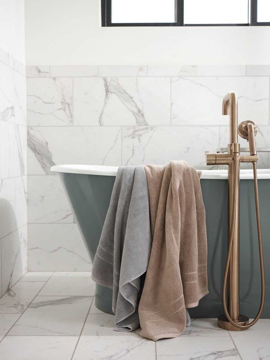 Premium Plush Bath Towels in the color Sand and Harbor Mist. Photo of Sand and Harbor Mist Premium Plush Bath Towels taken draped over a bathtub.