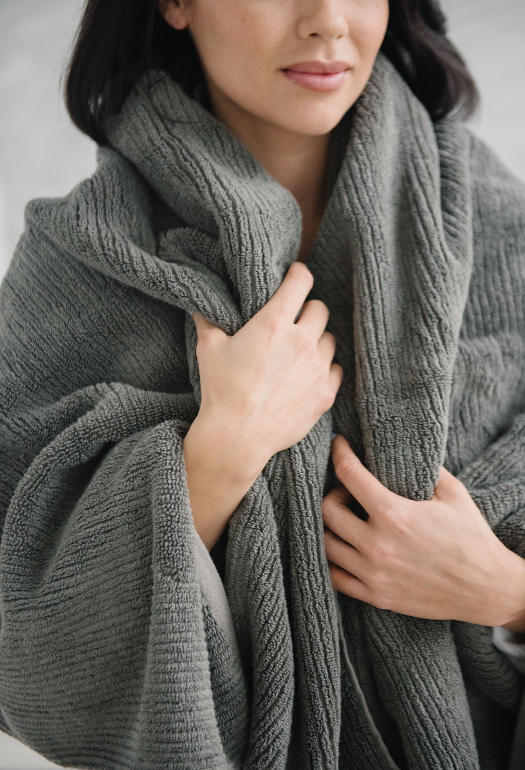 Ribbed Terry Bath Sheets in the color Charcoal. Photo of product taken in a bathroom as a woman wears the towel. 