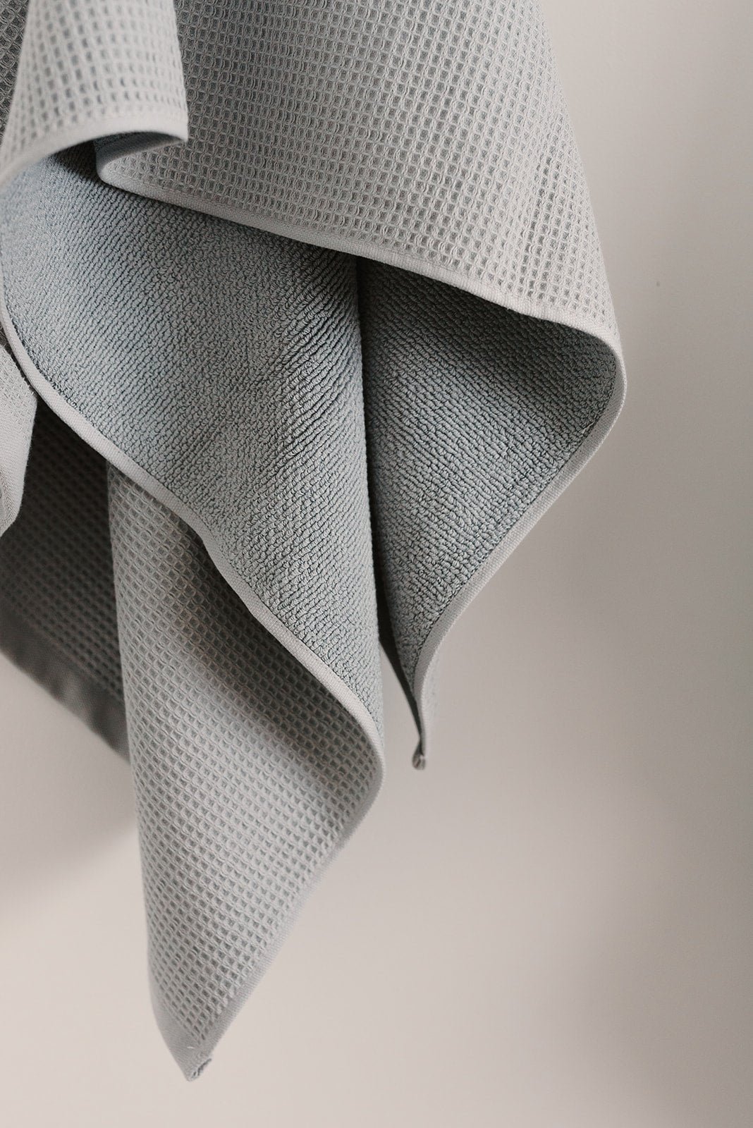 Waffle Bath Towel in the color Harbor Mist. Photo of Harbor Mist Waffle Bath Towel taken with Harbor Mist Waffle Bath Towel hanging from towel hook in a bathroom with white wall background 