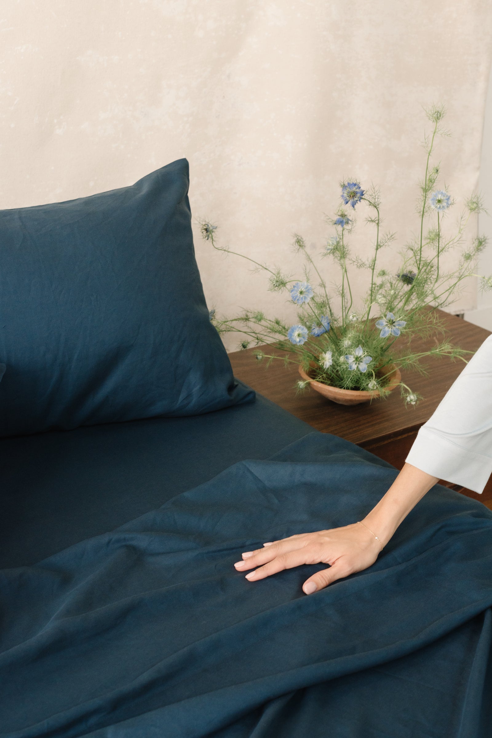 Navy Bamboo Linen Pillow Cases on a bed. A woman is running her hands along the bed. 