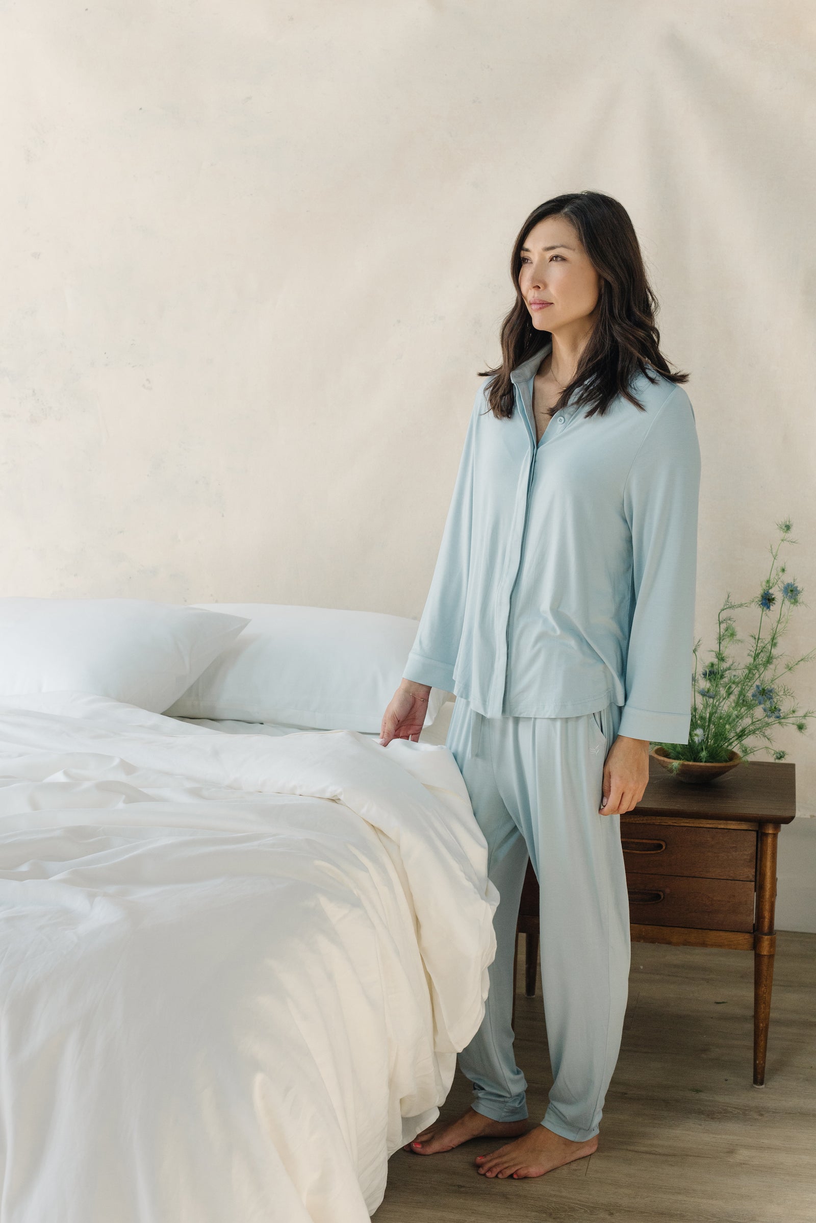 White Bamboo Linen Pillow Cases on a navy bed. A woman in pajamas is standing next to the bed.