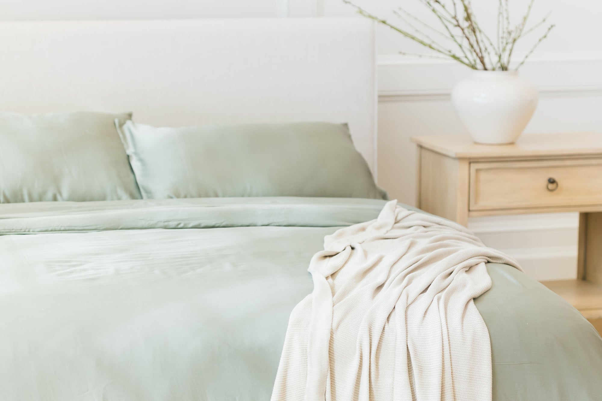 Bed made with sage bedding with cloud knit blanket draped on top 
