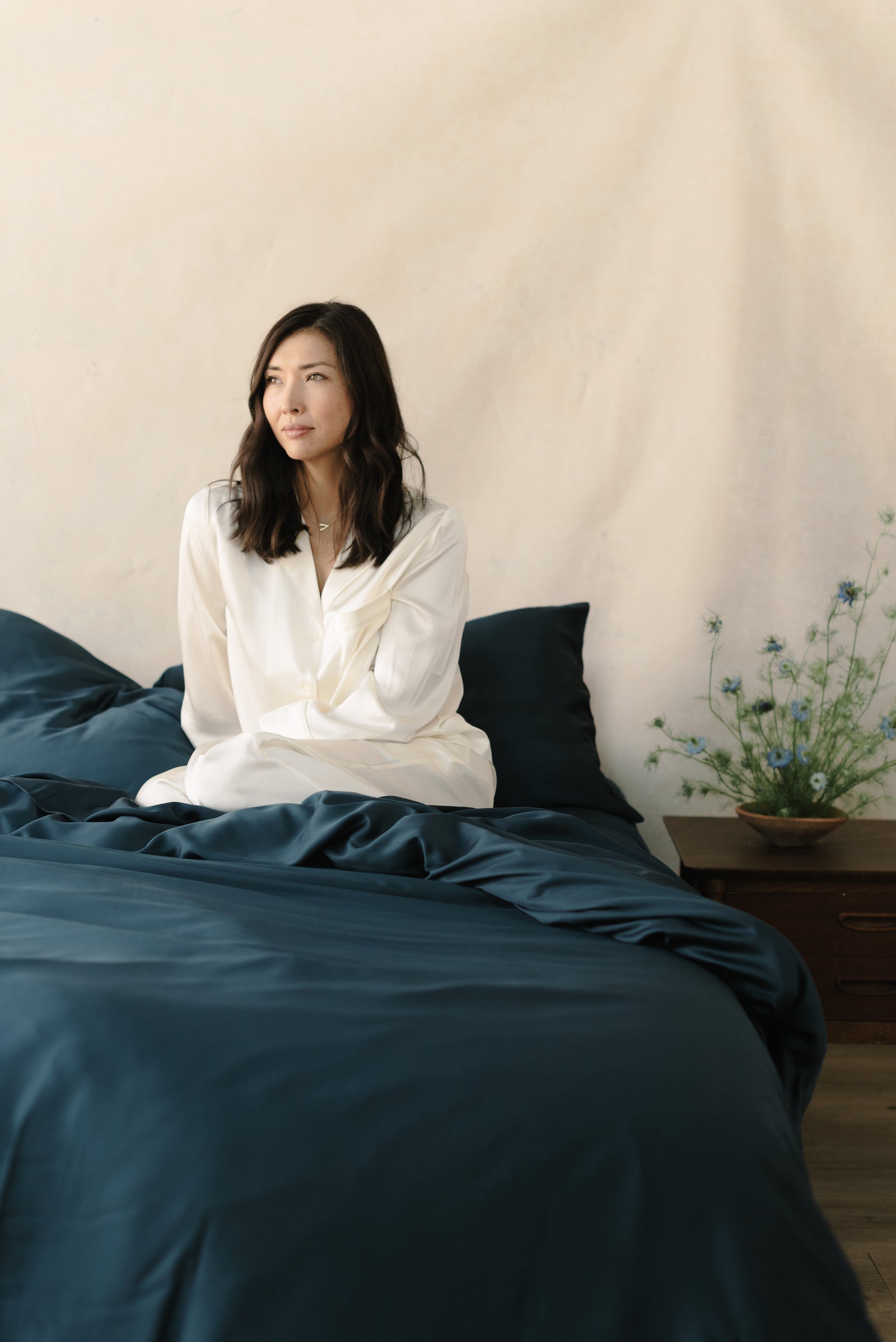 Woman in white pajamas sitting in bed with navy bedding 