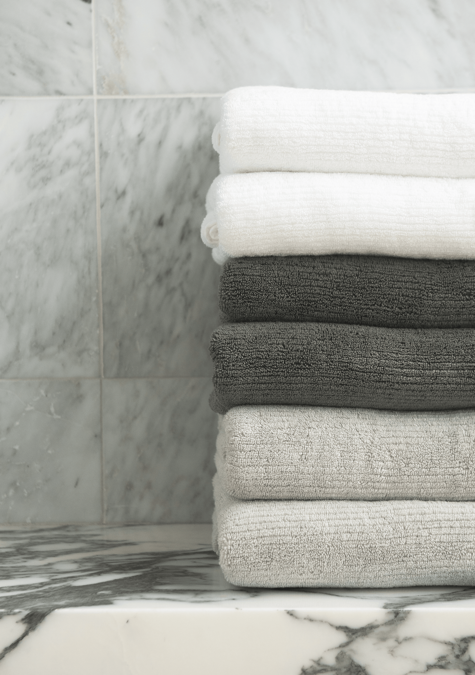 Ribbed Terry Hand Towel in the colors Light Grey, Charcoal, and White. Photo of Ribbed Terry Hand Towel taken with the Ribbed Terry Hand Towel resting on a bathroom sink.