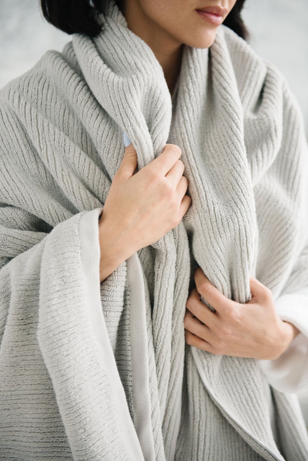 Ribbed Terry Bath Sheets in the color Light Grey. Photo of product taken in a bathroom as a woman wears the towel. 