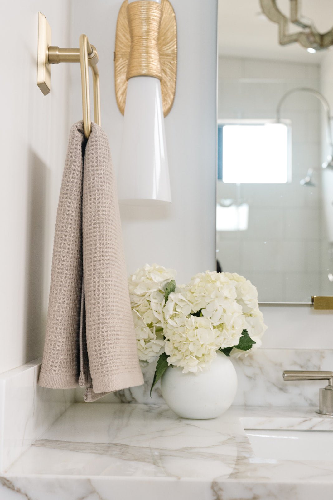 Sand Waffle Hand Towel hanging from a gold towel ring. The photo was taken at a white marble bathroom sink. 