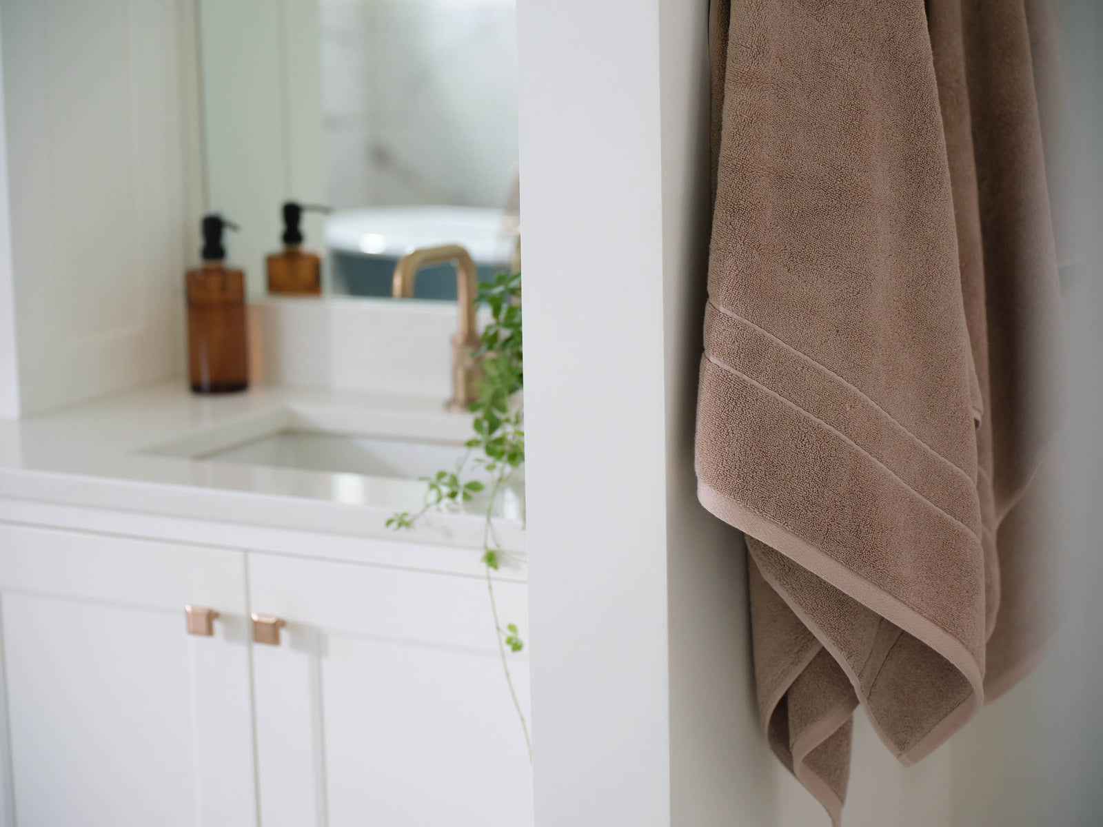Premium Plush Bath Towel in the color Sand. The towels are hung from a towel hook on the wall of a bathroom. 