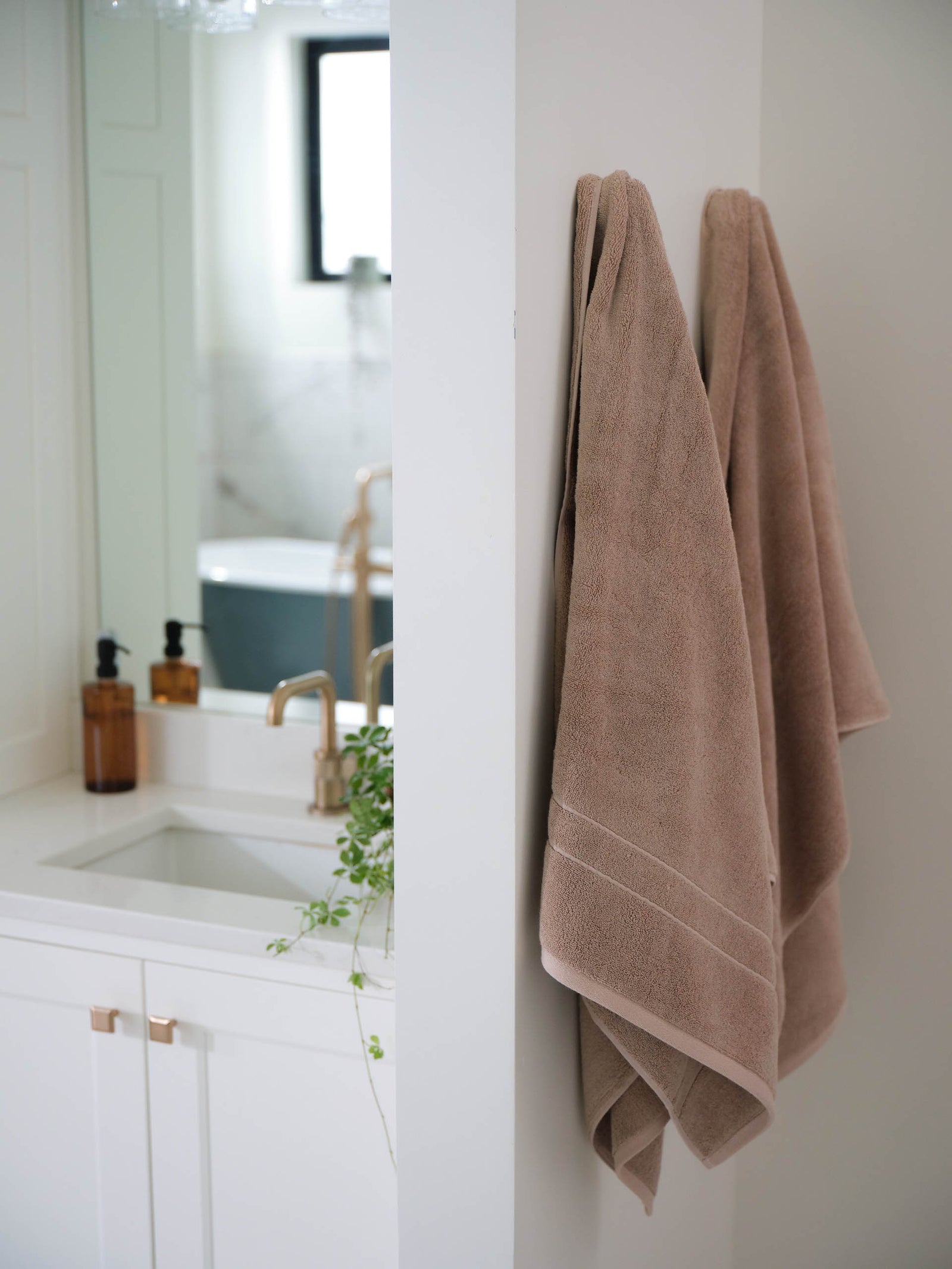 Premium Plush Bath Towel in the color Sand. The towels are hung from a towel hook on the wall of a bathroom. 