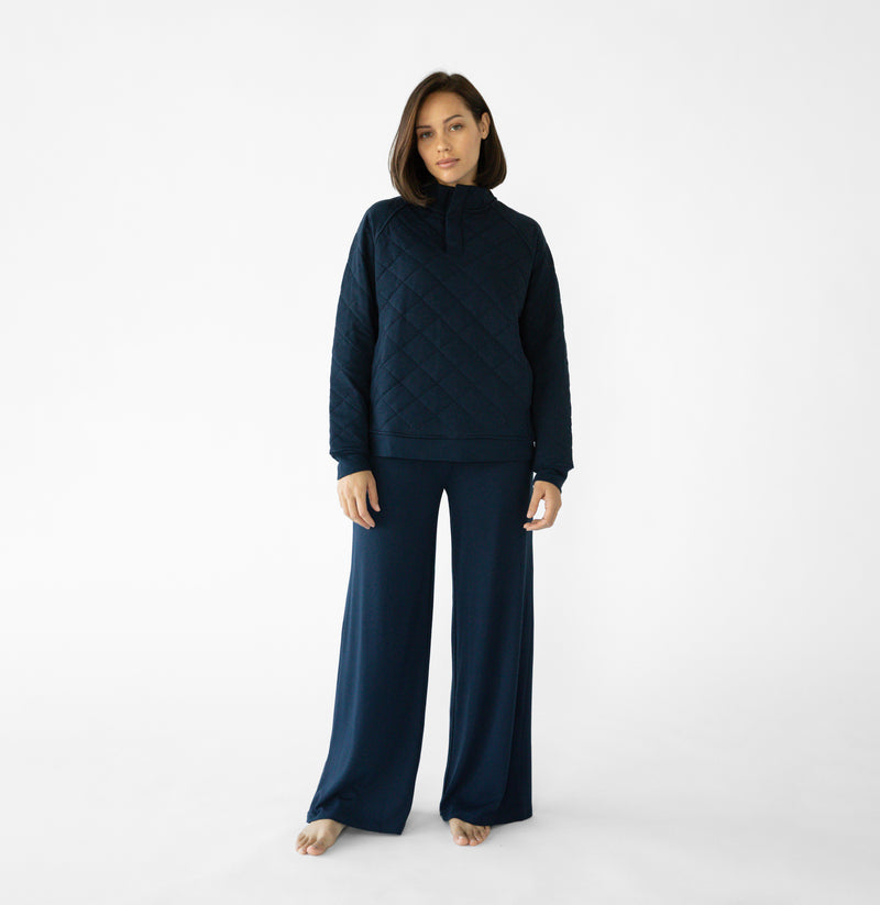 A woman stands in a relaxed pose wearing a navy loungewear set from Cozy Earth, featuring the Women's Ultra-Soft Bamboo Wide Leg Pull On Pant TALL and a matching hooded sweatshirt.